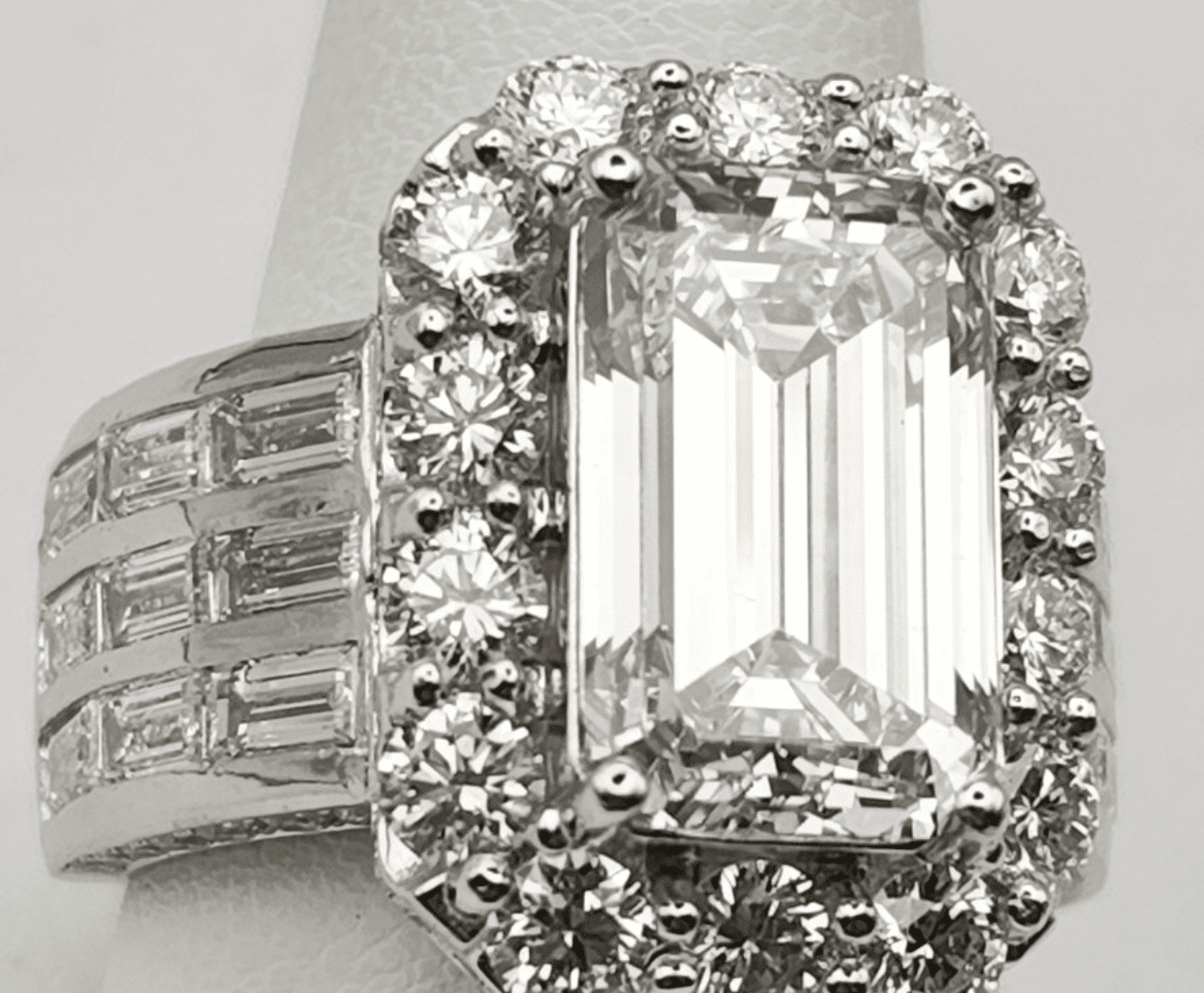 A close-up of an emerald-cut diamond ring with halo setting and side stones